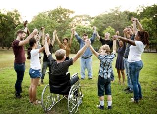 A group of people reflecting diverse ages and races stands in a circle, clasps one another's hands in unity and raises them to the sky