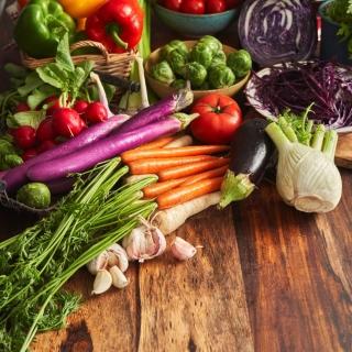 A wood table features a display of various fresh, colorful garden vegetables