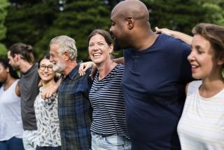 A group of smiling men and women with arms embraced behind their shoulders