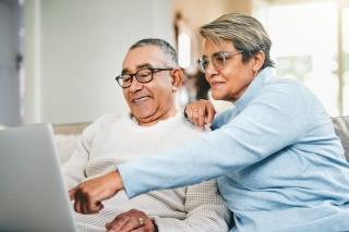 A husband and wife view a laptop together while sitting on their couch