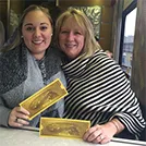young white woman and older white woman embracing, smiling and holding yellow tickets