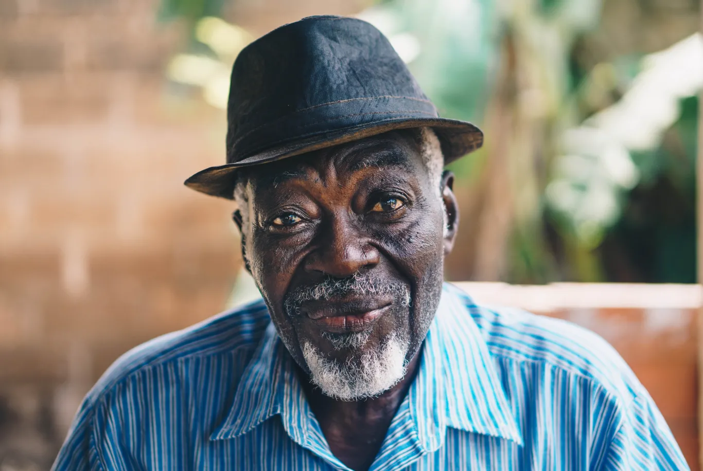 An African American elderly man wearing a hat smiles from his seat on his porch