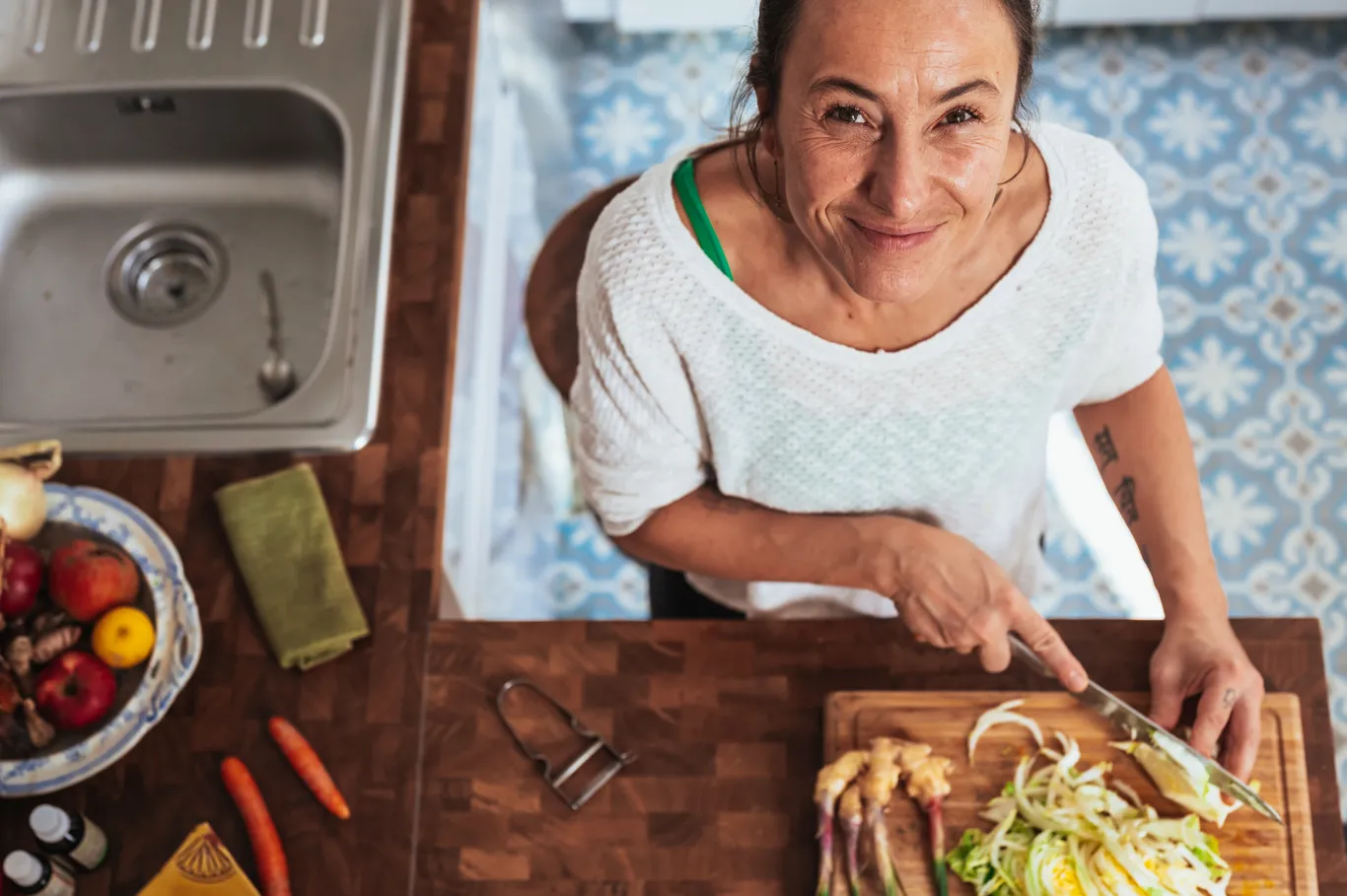 A woman smiles while chopping vegetables on a cutting board in her kitchen