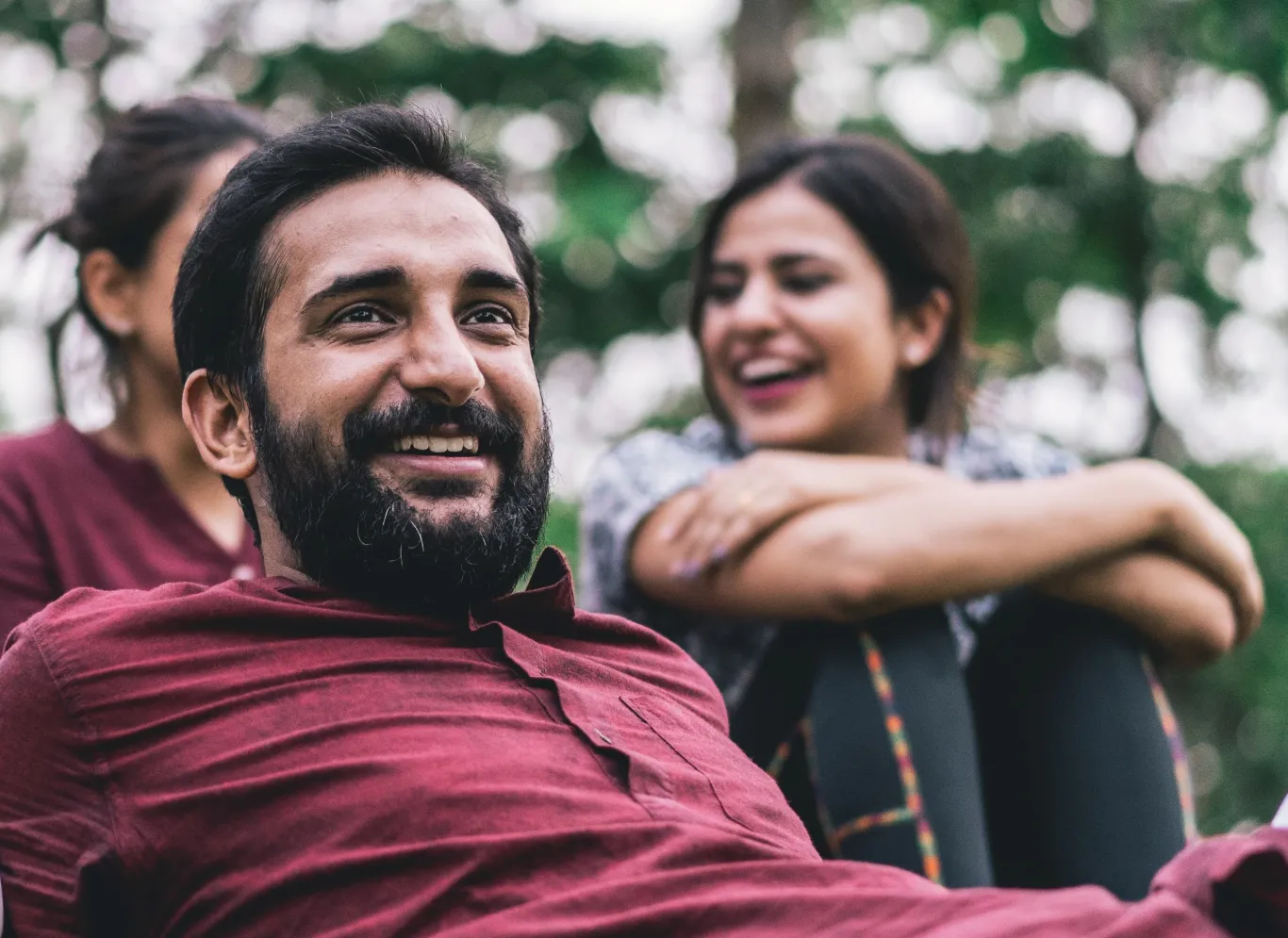 A man lies in the grass at a park and smiles with friends