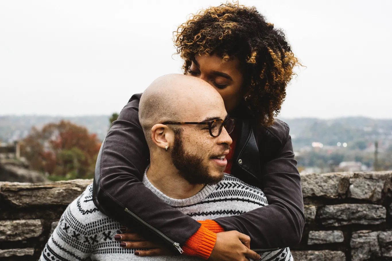 An African American couple snuggles in front of a tree-lined backdrop