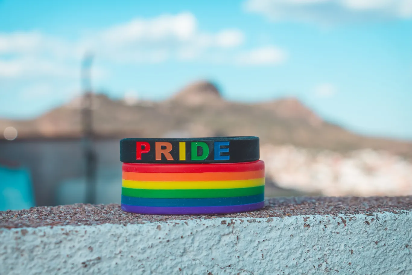 Pride Month wristbands rest on a stone wall beneath a blue sky