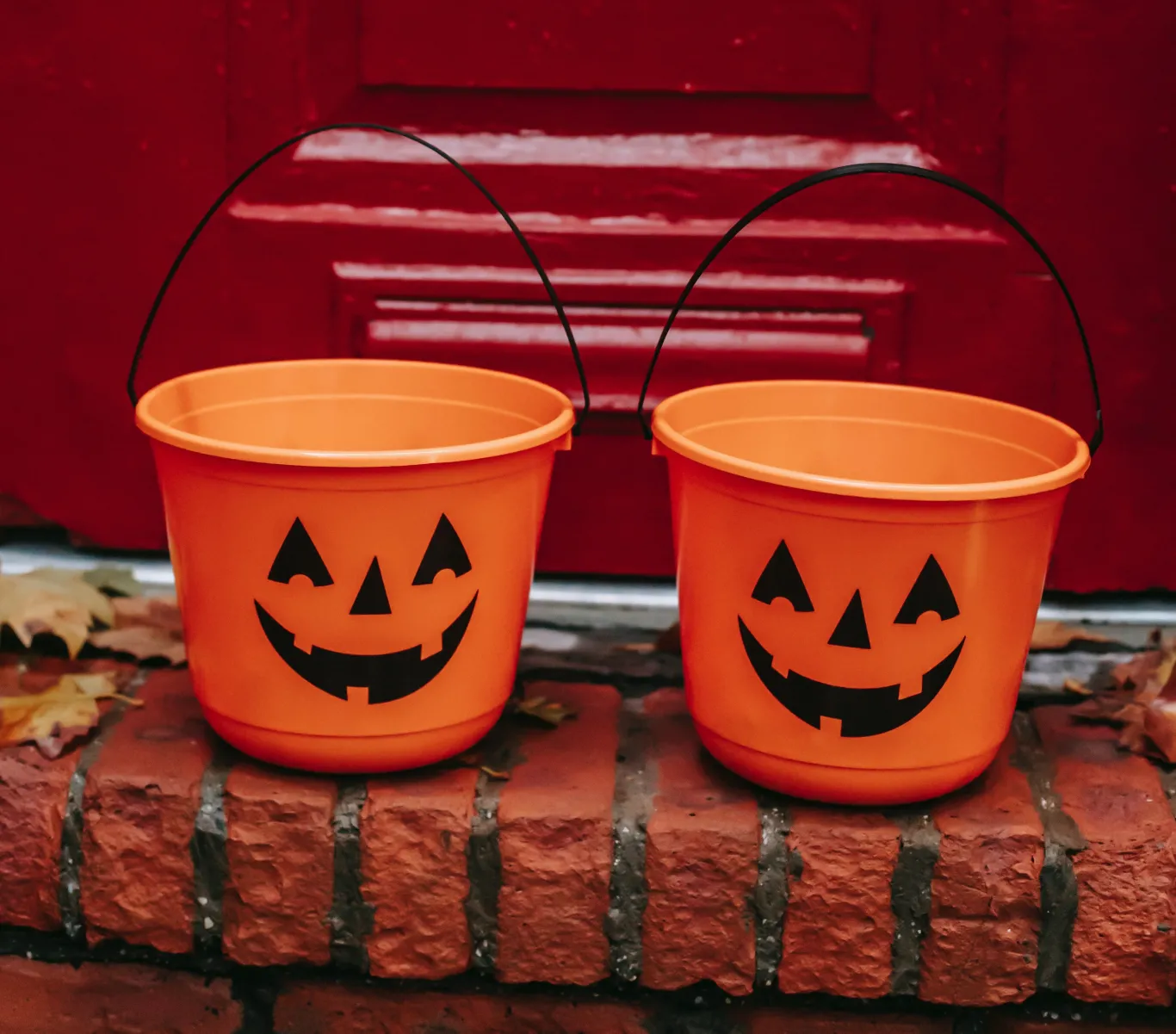 Two trick-or-treating candy buckets with jack-o'-lanterns rest on a doorstep