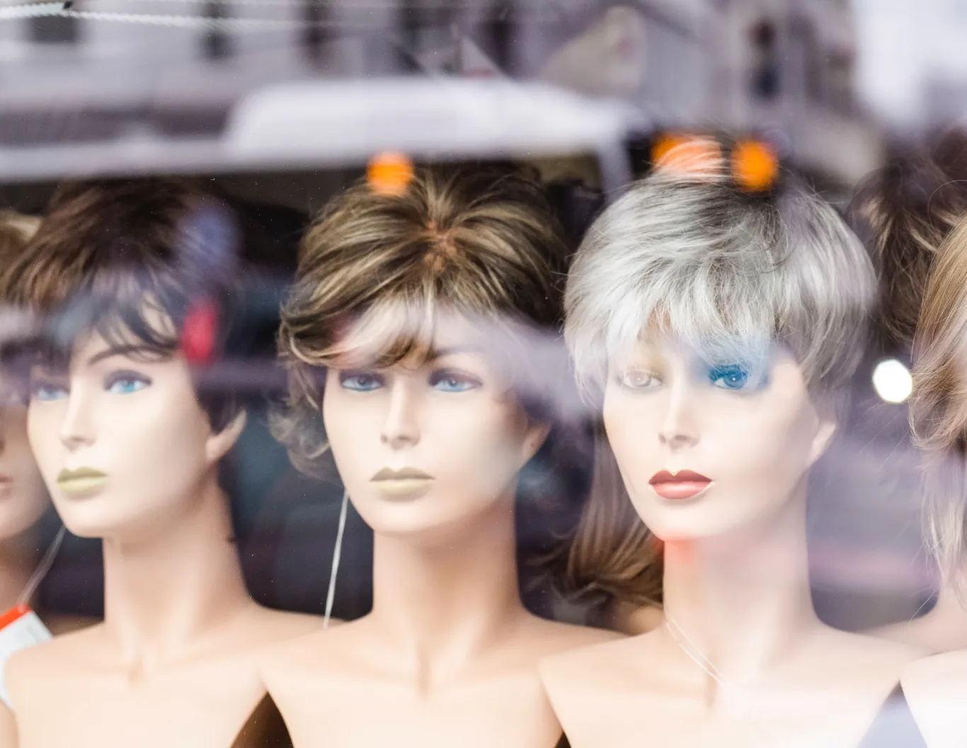 A store window features women mannequin heads with different wig styles