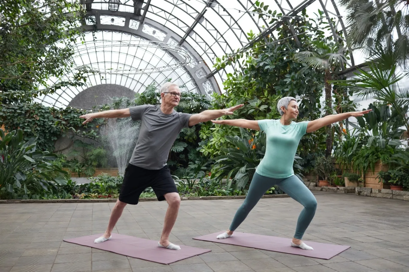 A senior couple stretch out on their yoga mats in an indoor arboretum