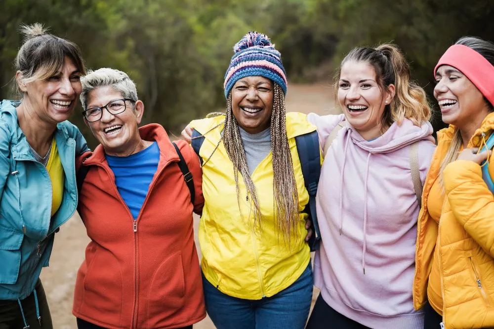 A diverse group of women smiling in jackets outdoors with their arms around one another