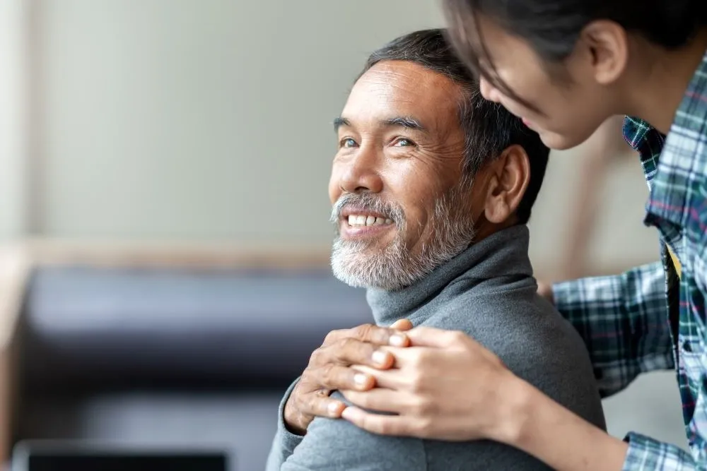 A woman gently rests her hand on a man's shoulder in a comforting way