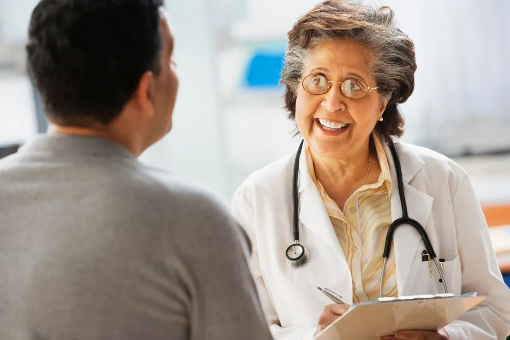 A smiling woman doctor in a white lab coat speaks with a patient