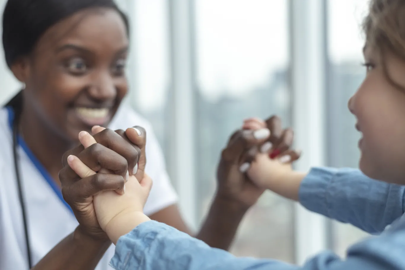 A child and a doctor hold hands and smile at each other