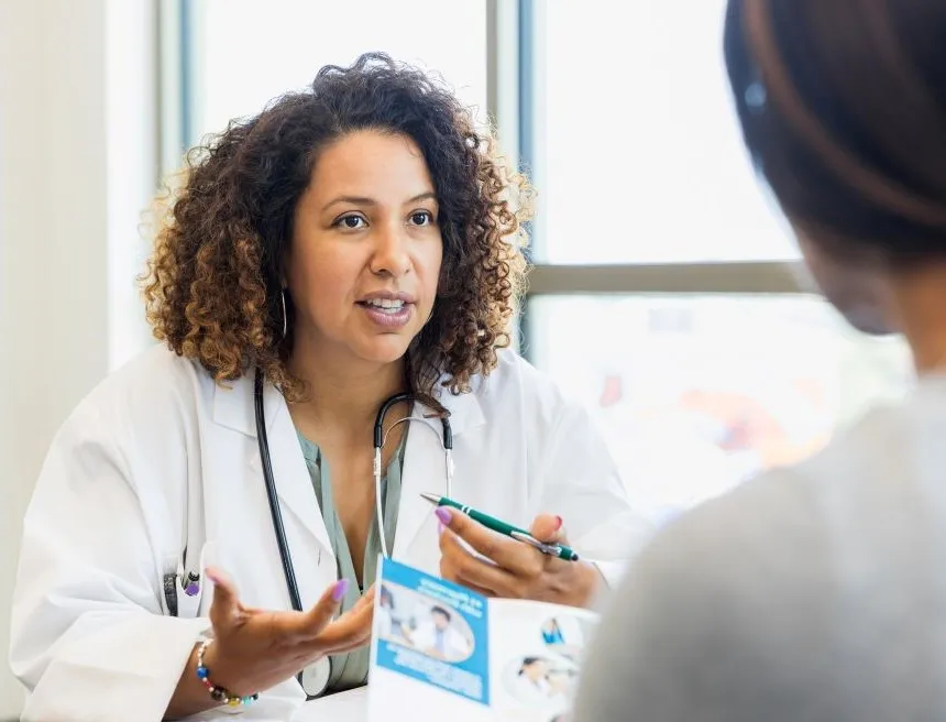 A female doctor talks with an unseen young woman holding a patient information brochure