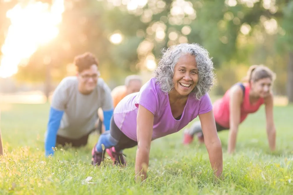 A small group of people do pushups in the grass at a park