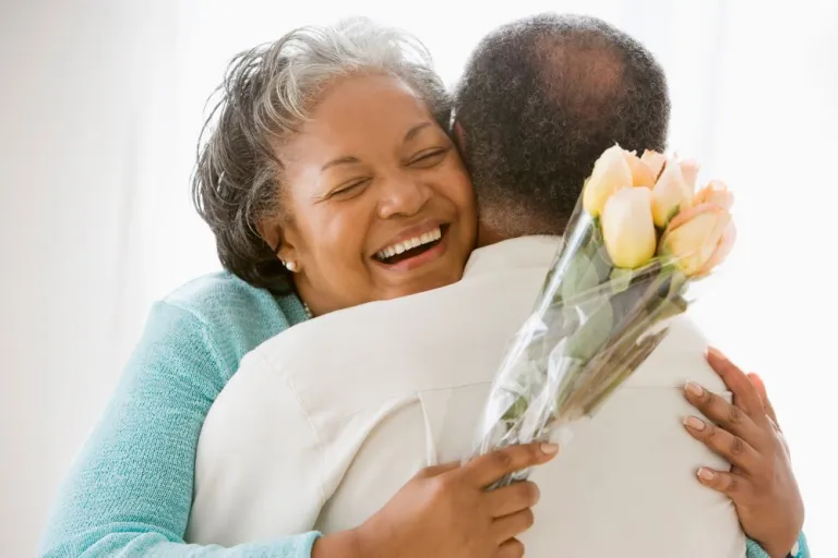 A woman smiles and hugs a man as she holds a bouquet of roses