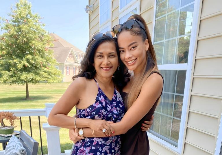 Cassie and her mom smile and embrace side by side outside on a patio