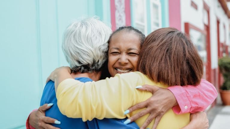 Three women give one another a friendly hug on a sidewalk