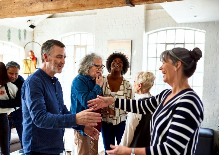 A friendly gathering of mature adults greets one another with hugs and conversation