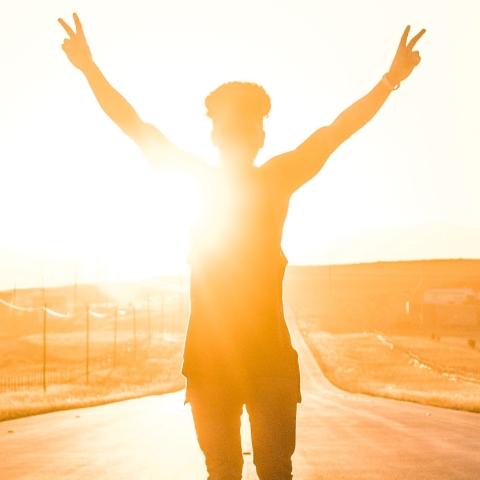 A women's silhouette shines against a sunny horizon as she raises her arms triumphantly in the air