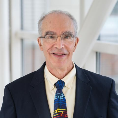 Dr. Stephen Edge wears a suit and tie and smiles beside a window within a modern building