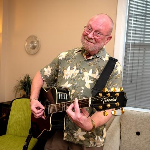 Terry smiles while playing the guitar in a bright-lit room