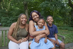 black family with two young kids sitting on a park bench smiling