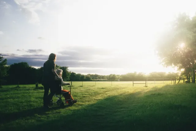 female pushing older person in wheelchair in field