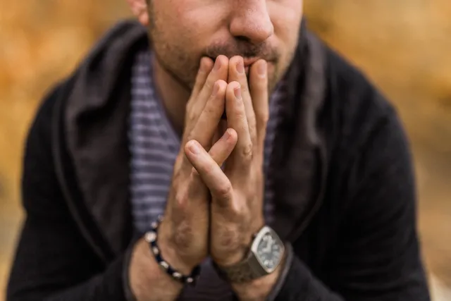 A man looks pensive as he sits with his hands folded under his chin