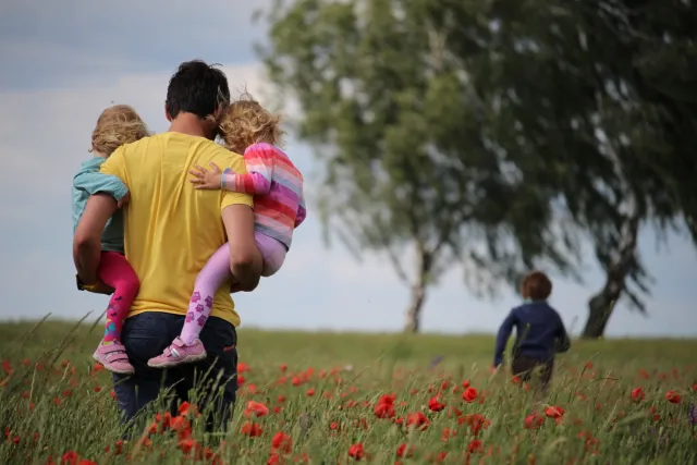 A young father holds his two children in his arms in a field of flowers