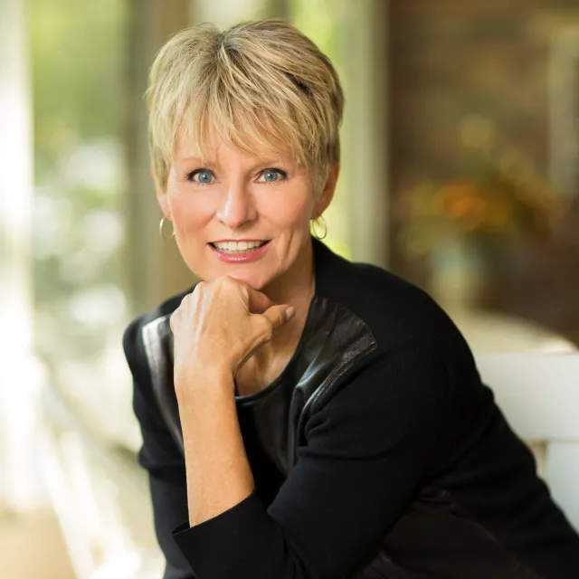 Cancer survivor, author, and survivorship advocate Judy Pearson smiles with her chin resting on her hand 