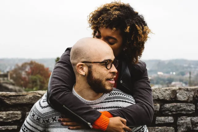 An African American couple snuggles in front of a tree-lined backdrop