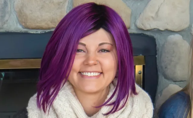 Amber smiles from inside her home with bright purple hair.