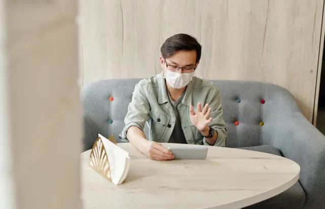 A young man wearing a mask speaks to someone on his mobile phone while sitting at home