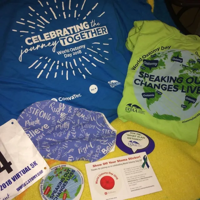 Blue and green ostomy awareness shirts, buttons, and other items are laid out.