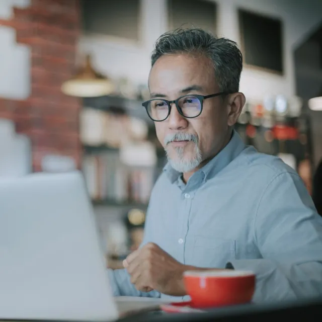 A man wearing glasses works on his laptop.