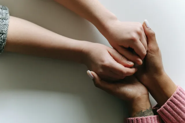 A woman's hands comfortingly hold the hands of a friend