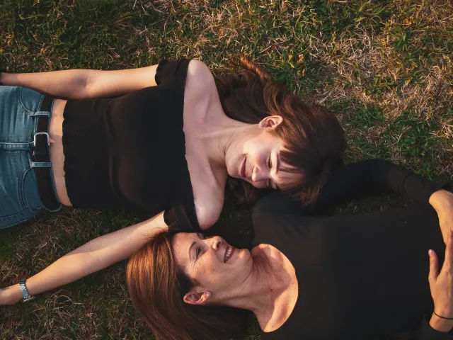 A mother and daughter lie beside each other in the grass smiling.