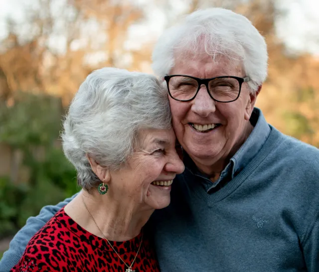 An elderly couple laughs and snuggles together outside