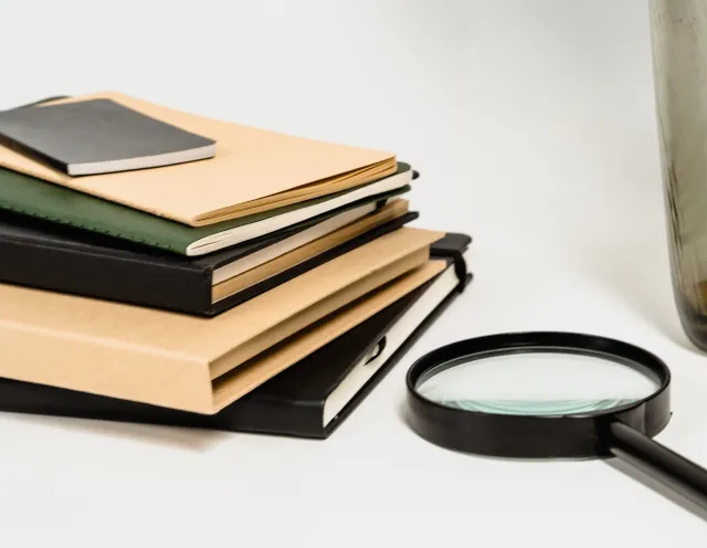 A magnifying glass rests next to a stack of books on a white table