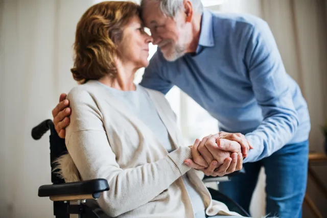 Senior couple at home with husband caring for wife in wheelchair