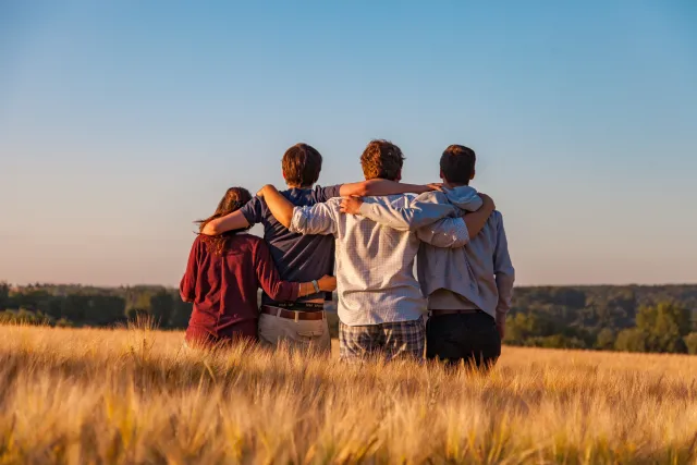 Friends stand side by side with their arms around one another, looking out at a blue sky