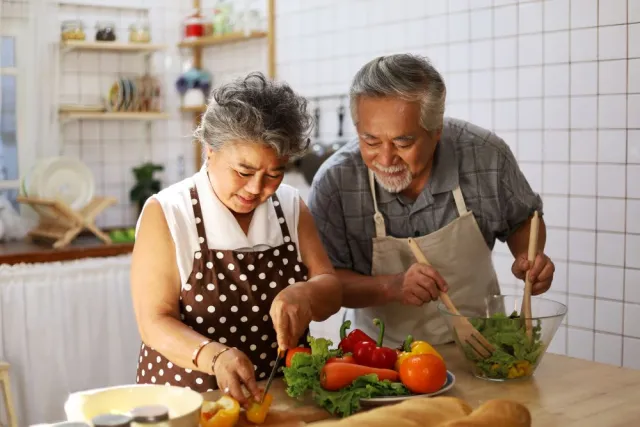 A couple wearing aprons prepares a salad together in their kitchen