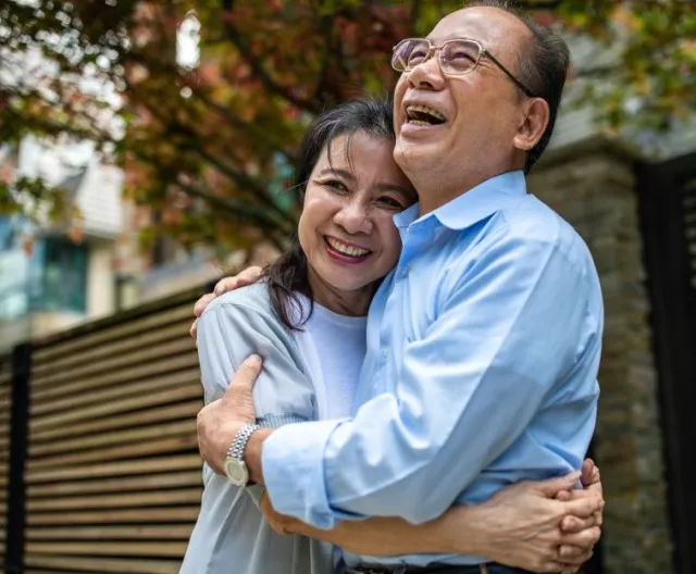 A senior couple smiles and embraces each other outside their home 