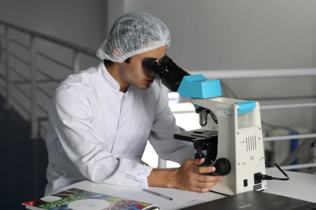 a man wearing a lab coat peering into a desktop microscope