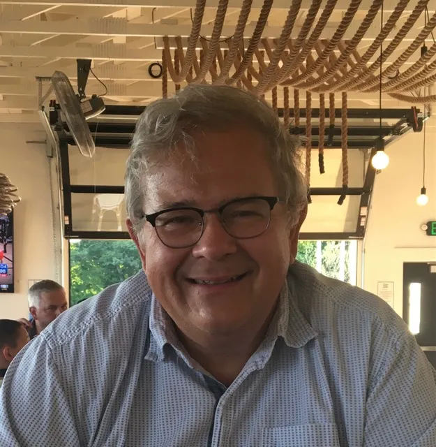 Michael Kolodziej, M.D., smiles in a sunlit interior wearing glasses and a collared shirt 