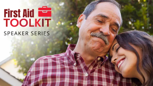 A daughter smiles and rests her head on her father's shoulder in front of a tree