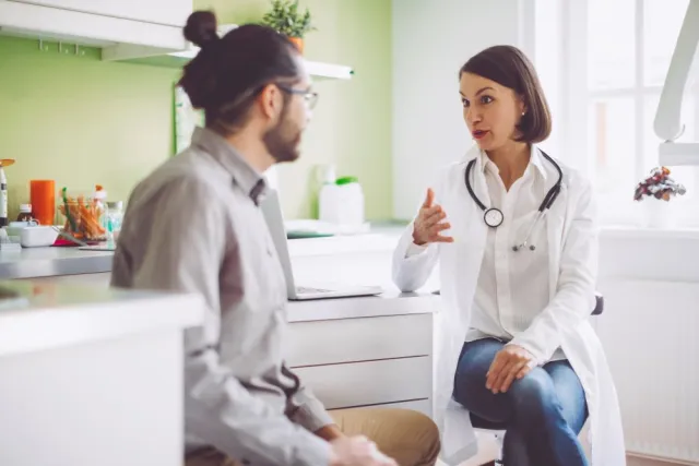 A doctor in a white lab coat speaks with a man in a doctor's office