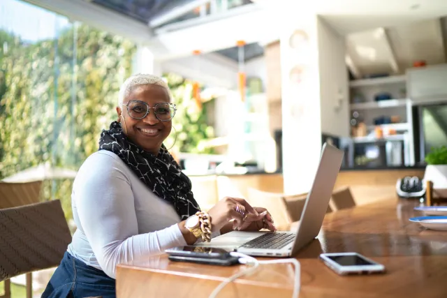 a smiling black woman in a sunny, cheerful room seated at a laptop