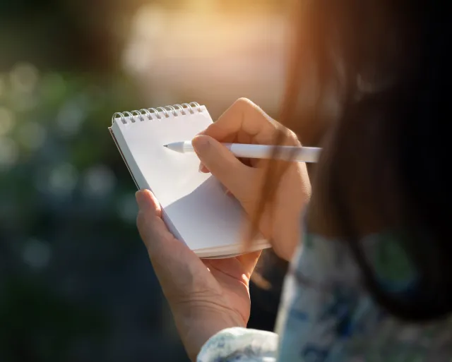 A woman sitting in the sunshine gets ready to take notes in a blank notebook
